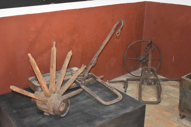 Interior del museo con herramientas antiguas y maquinaria agrícola en paredes rojas, sin figuras visibles.