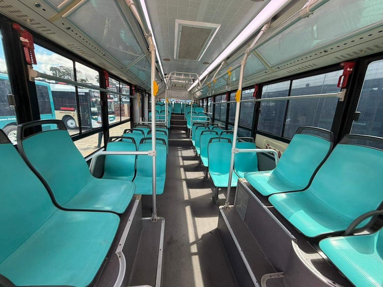 Interior de un bus eléctrico vacío, con asientos turquesa y ventanas que dejan ver otro bus estacionado.