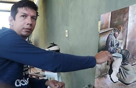 Claudio Bareiro, en sudadera azul, concentra su atención en un cuadro que representa a un hombre en una posición vulnerable, en un ambiente tranquilo.