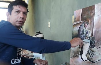 Claudio Bareiro, en sudadera azul, concentra su atención en un cuadro que representa a un hombre en una posición vulnerable, en un ambiente tranquilo.