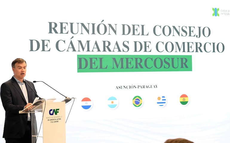 Ricardo Dos Santos con chaqueta oscura habla tras podio con logo de CAF, sorprendido, en reunión formal con gran cartel detrás.