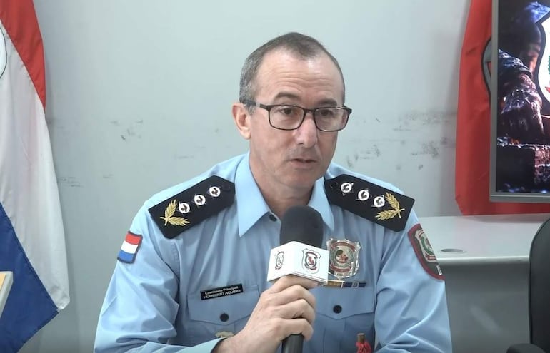 Comisario Humberto Aquino en uniforme celeste, sentado y sosteniendo un micrófono, en un ambiente formal con bandera de Paraguay.
