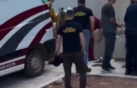 Grupo de personas en ropa informal y un bombero en traje amarillo, cerca de una ambulancia roja y blanca, en una escena de rescate.