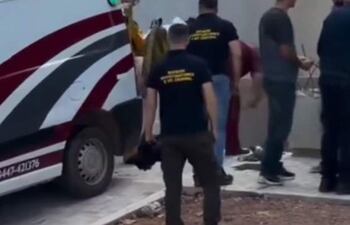 Grupo de personas en ropa informal y un bombero en traje amarillo, cerca de una ambulancia roja y blanca, en una escena de rescate.