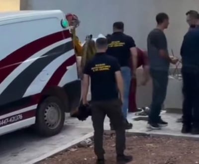 Grupo de personas en ropa informal y un bombero en traje amarillo, cerca de una ambulancia roja y blanca, en una escena de rescate.