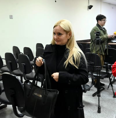 Ana Girala con abrigo negro y bolso, entrando a una sala vacía, mostrando expresión neutral.