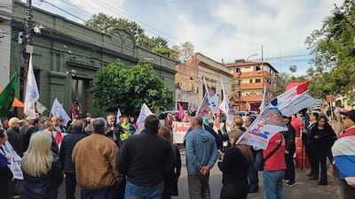 Personas de diversas edades, algunas con banderas y carteles, escuchan un orador en una manifestación pacífica por derechos laborales.
