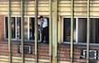 Persona en ventana con camisa a rayas y abrigo oscuro, ajustando una bufanda en un edificio durante un incendio.