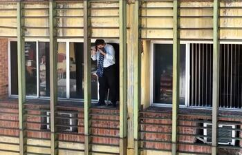 Persona en ventana con camisa a rayas y abrigo oscuro, ajustando una bufanda en un edificio durante un incendio.