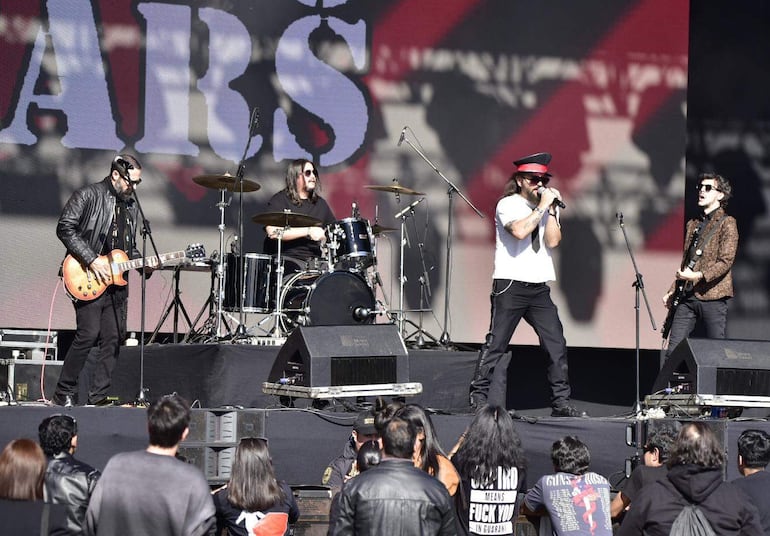 Vocalista con camiseta blanca y gorro rojo en el centro, guitarrista de negro a la izquierda, batería y guitarrista con chaqueta animal a la derecha.
