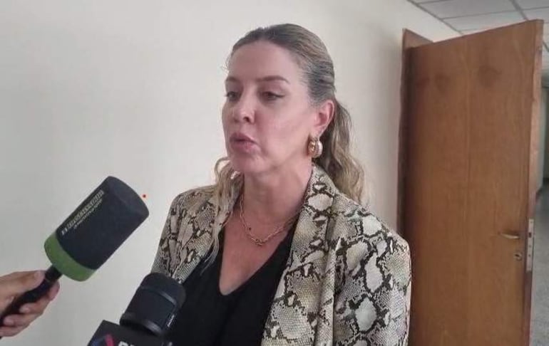 Belinda Bobadilla con chaqueta de serpiente, de pie y hablando, rodeada de micrófonos en ambiente de oficina.