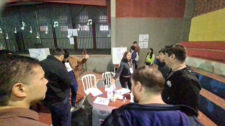 Hombre de chaqueta oscura sostiene un documento mientras discute con mujer en chaqueta negra en medio de un ambiente electoral.