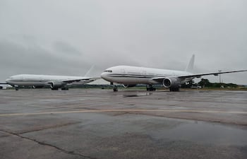 Dos aviones Boeing 767 blancos en un aeropuerto con cielo nublado y pavimento húmedo, sin personas visibles.