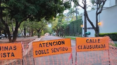 Calle cerrada con carteles naranjas que indican 'ATENCIÓN Doble Sentido' y 'CALLE CLAUSURADA', rodeada de árboles frondosos.