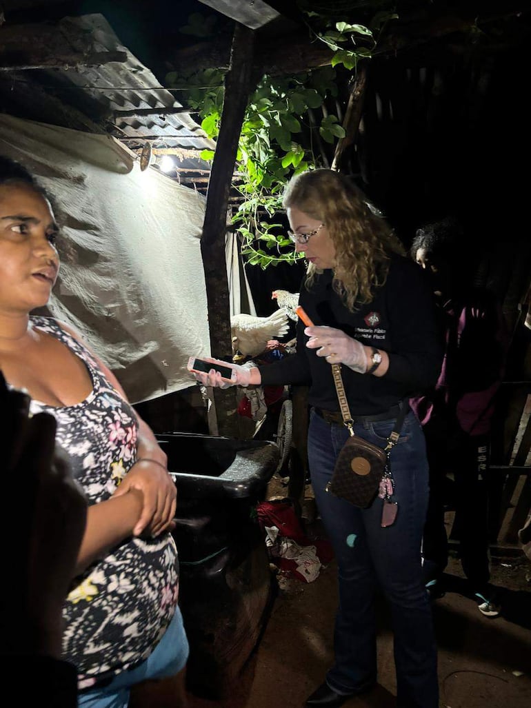 Tres mujeres en entorno oscuro, una con camiseta floral y otra con guantes de látex, sosteniendo un dispositivo móvil.