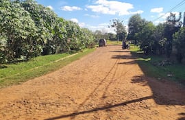 Calle rural de tierra flanqueada por vegetación, con un vehículo y motocicletas estacionadas, bajo un cielo mayormente despejado.