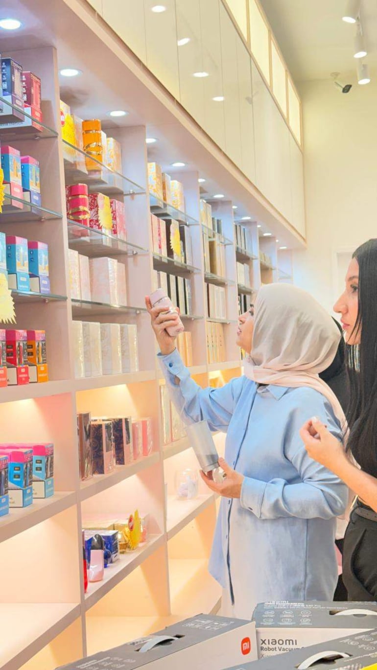 Dos mujeres, observan estantes llenos de perfumes en una tienda.