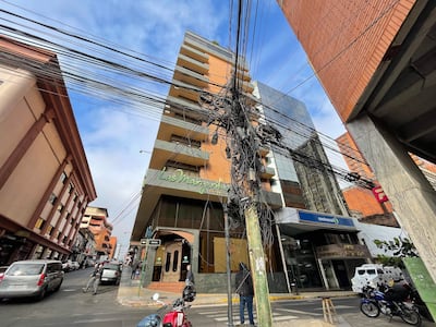 Poste de electricidad con cables, edificios clásicos y modernos, y una motocicleta estacionada en una calle desierta.