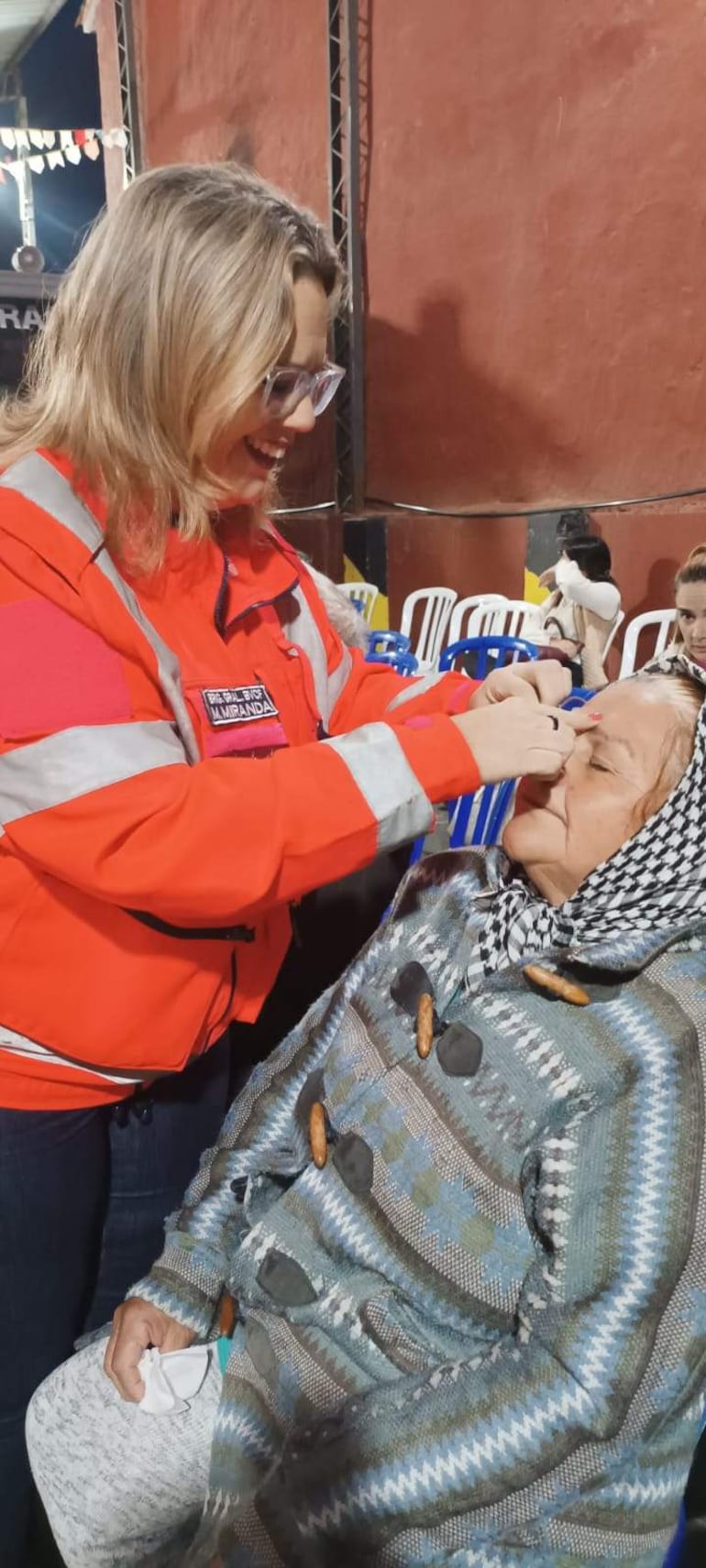 La presidenta del Cuerpo de Bomberos Voluntarios de Carapeguá, Marta Miranda, ayuda a una paciente a retirar la venda de su ojo.