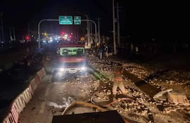 Camión de bomberos en la escena del accidente, con escombros en el pavimento y una multitud observando en el fondo.