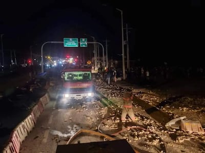 Camión de bomberos en la escena del accidente, con escombros en el pavimento y una multitud observando en el fondo.