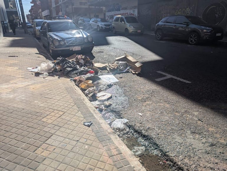 Coche estacionado junto a residuos acumulados en la acera, reflejando desorden urbano y falta de limpieza.