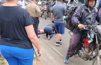 Hombre tendido en el suelo con herida en la pierna, rodeado por testigos y un motociclista con casco atento a la situación.