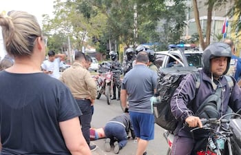 Hombre tendido en el suelo con herida en la pierna, rodeado por testigos y un motociclista con casco atento a la situación.