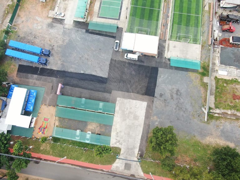 Área exterior de instalaciones deportivas con césped bien cuidado, camiones de carga estacionados y estructuras para niños.