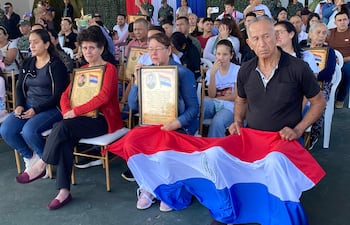 Homenaje en Arroyito con personas solemnemente sentadas, retratos enmarcados y bandera paraguaya al centro.