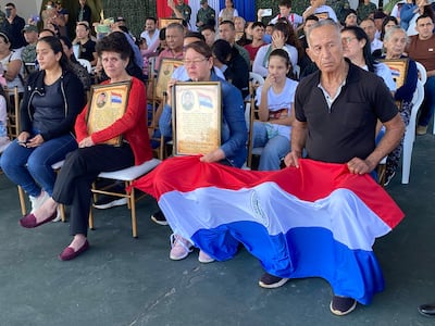 Homenaje en Arroyito con personas solemnemente sentadas, retratos enmarcados y bandera paraguaya al centro.