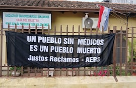 Fachada de la Casa del Maestro con un gran cartel negro que dice 'UN PUEBLO SIN MÉDICOS ES UN PUEBLO MUERTO' y una bandera paraguaya.