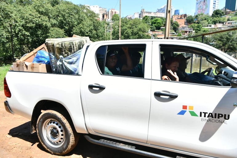 Personas en camioneta blanca de Itaipu Binacional, un hombre conduce y una mujer saluda a la cámara mientras llevan objetos en la parte trasera.