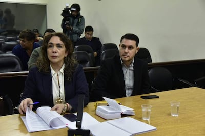 Hernán Rivas en camisa a rayas y saco negro, junto a Alba Zaracho con blazer oscuro, en una sala con documentos sobre la mesa.