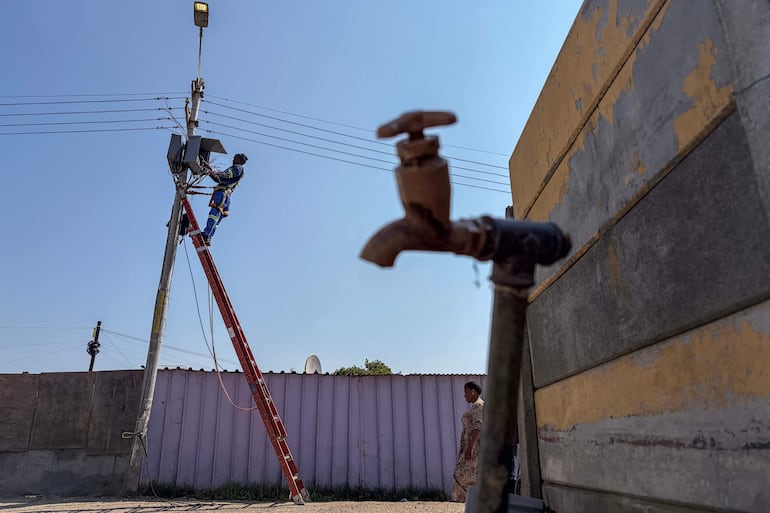 Un trabajador de Eskom, la empresa nacional proveedora de electricidad, trabaja en una farola junto a un grifo comunitario en el asentamiento informal de Barcelona, en Gugulethu, Ciudad del Cabo, el 7 de septiembre de 2026.