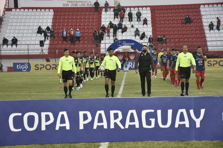 Los árbitros y los jugadores del Atlético Trébol (i) y Fernando de la Mora ingresan al campo para el partido de la Copa Paraguay 2021 en el estadio Isidro Roussillón, en la ciudad de Villa Hayes.
