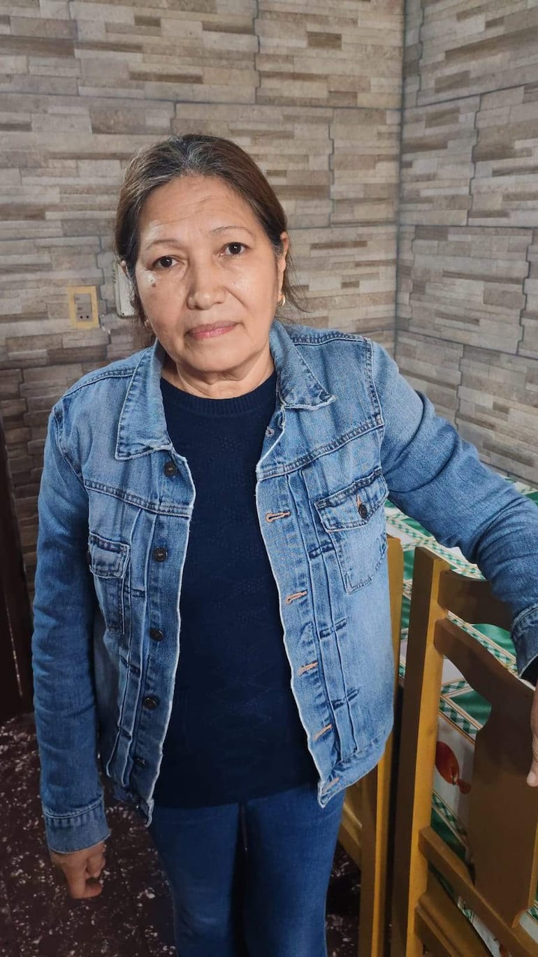 Mujer con chaqueta de mezclilla y suéter oscuro, de pie en un interior serio, mirando hacia la cámara en ambiente doméstico.