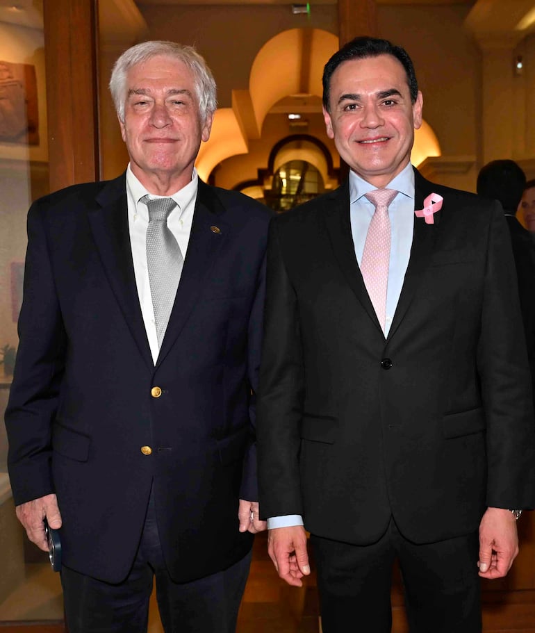 Rubén Ramírez Lezcano y Carlos Jorge Biedermann posan en traje en un evento formal, con ambiente moderno y bien iluminado.