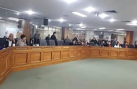 Hombres y mujeres en sala de tribunal, algunos conversando y otros escuchando atentamente en un ambiente formal.