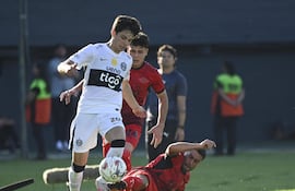El joven volante ofensivo de Olimpia Eduardo Delmás deja en el camino la barrida de Federico Carrizo de Libertad.