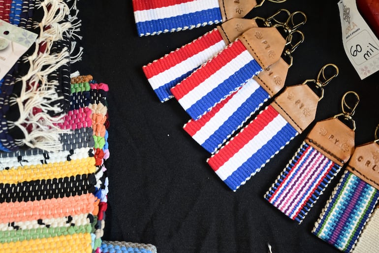 Variedad de llaveros artesanales en rojo, blanco y azul sobre fondo negro, destacando los colores de la bandera paraguaya.