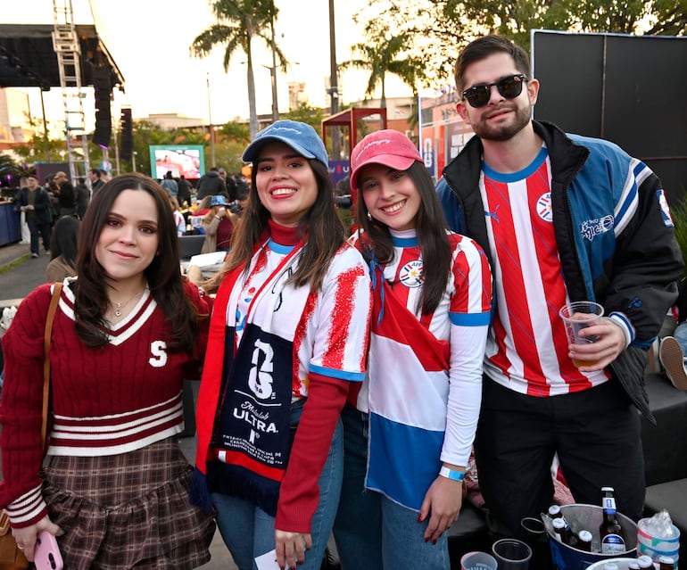 Grupos de personas luciendo camisetas de fútbol paraguayo, sonriendo y disfrutando al aire libre, rodeados de un ambiente festivo.