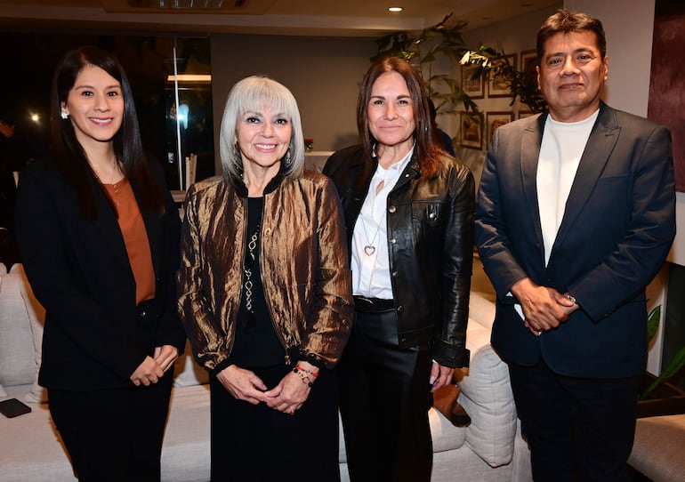 Mujer de cabello plateado sonriente en chaqueta brillante, junto a tres personas vestidas formalmente, en ambiente moderno y bien iluminado.