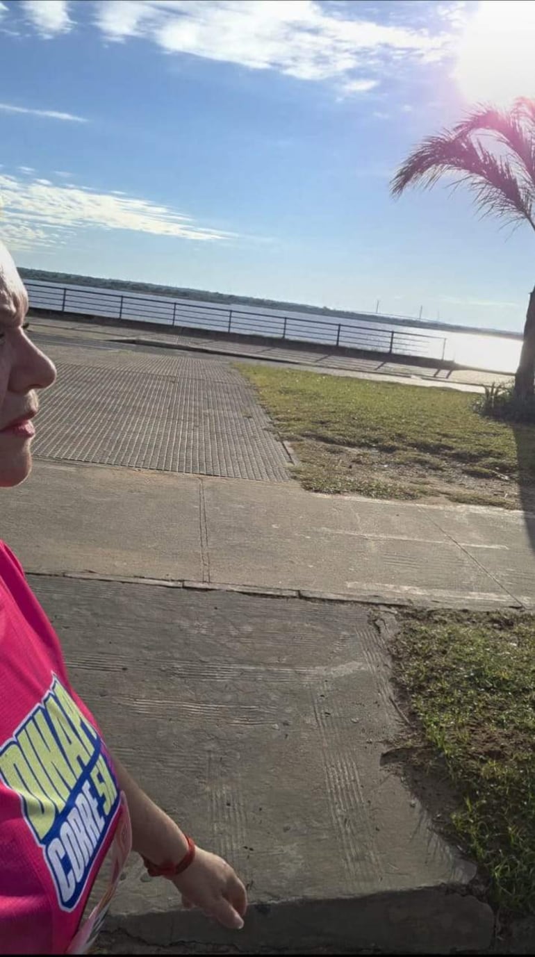 Mujer con camiseta rosa que dice 'Días de Correr', caminando en un sendero costero con árboles de fondo.