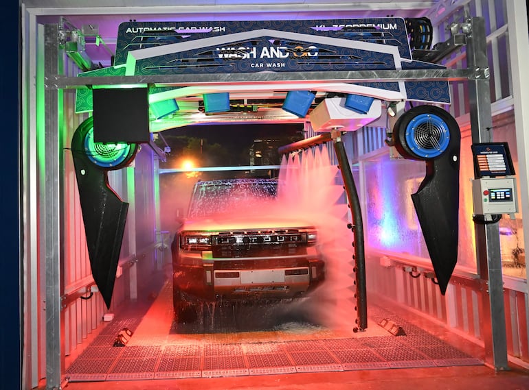 Hummer eléctrico en túnel de lavado automático con chorros de agua y luces de colores en un entorno vibrante.