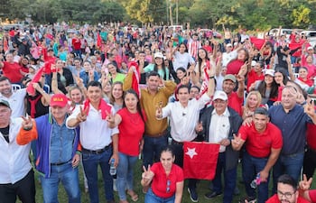 Juan Carlos Baruja rodeado de personas que muestran actitudes festivas, muchos con camisetas rojas y banderas en un ambiente animado.