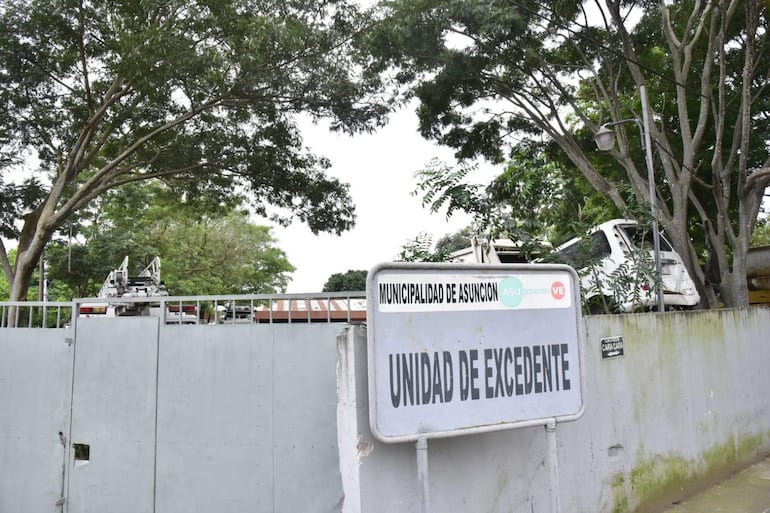 Vista exterior de la Unidad de Excedente de la Municipalidad, rodeada de árboles y camiones, sin personas visibles.