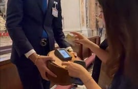 Hombre en traje oscuro brinda un objeto redondo a mujer con blusa oscura, en entorno formal sin emociones visibles.