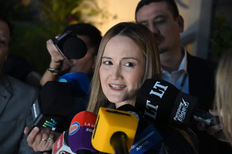 Soledad Núñez en el centro, con cabello lacio, respondiendo preguntas rodeada de micrófonos y periodistas atentos.