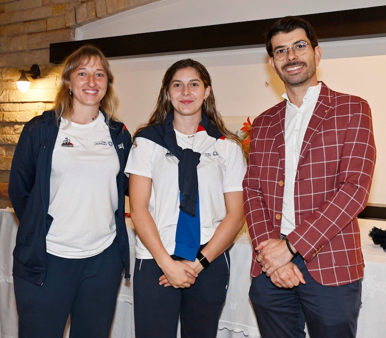 Mujer rubia sonriente con chaqueta oscura y camiseta blanca, joven castaña con chaqueta sobre los hombros, hombre con blazer a cuadros también sonriente.